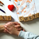 Two hands clasped together on a table with Scrabble tiles spelling out “Child Custody.” Clement Law.